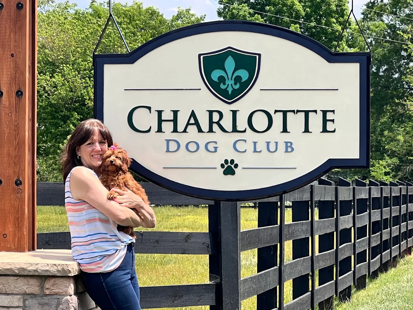 A woman holding a puppy beside the Charlotte Dog Club sign